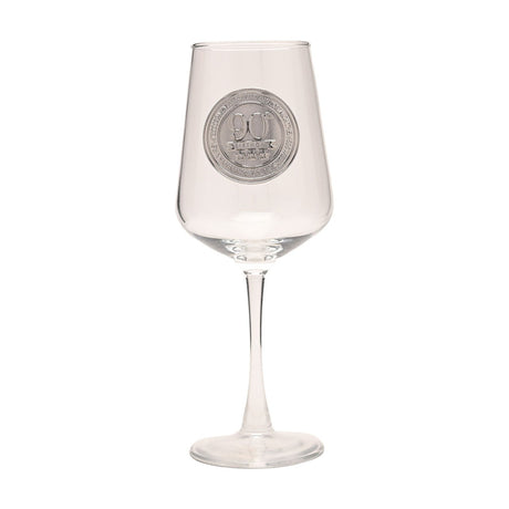 Clear stemmed wine glass with a round silver 90th Birthday badge on the bowl, tall slim stem, and round foot, shown on a plain white background.
