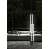 A modern living room with a light gray sofa, dark cushions, and the Mural LED Floor Lamp 48W 3000K in matt white stands by large glass windows overlooking lush greenery. A textured, patterned rug covers the floor.