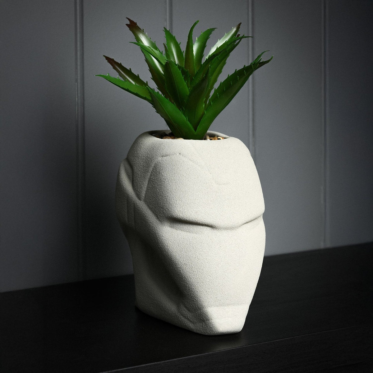 Iron Man Helmet planter in matt cement grey metal with raised brow and faceplate detail, holding a spiky faux plant on a dark surface.
