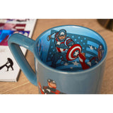 Blue porcelain Captain America mug with a decal inside the rim showing the hero in action with his shield, set on a wooden table.