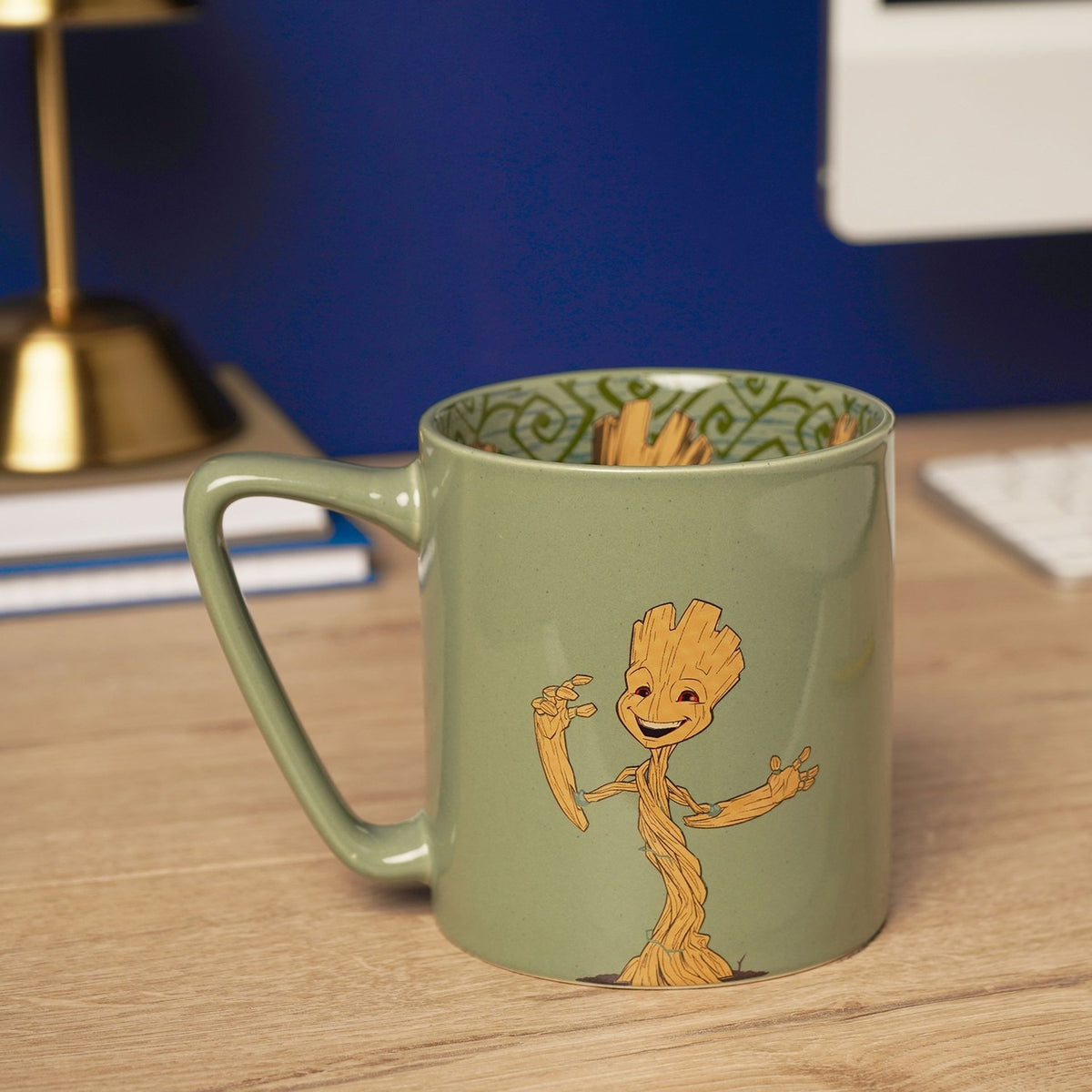 Green porcelain mug with handle featuring a wood-brown Groot illustration, shown on a desk with a patterned inside decal visible at the rim.