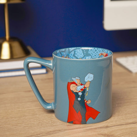 Blue porcelain Avengers Thor mug, 500ml, with comic-style Thor holding his hammer and a printed knotwork pattern inside, shown on a wooden desk.