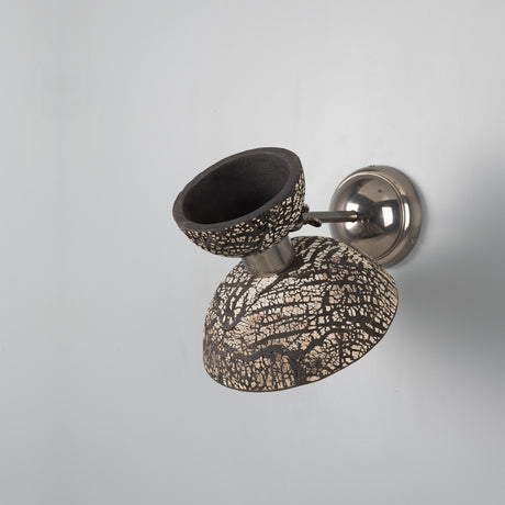 Nakaii Ceramic Wall Light in black clay with white crackled pattern, small cup over a wider dome, mounted on a polished silver arm and round wall plate, shown against a plain light grey background.