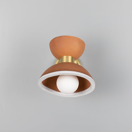 Nakaii ceramic wall light in terracotta with white-rimmed lower dome, hourglass shape, brass collar and arm, exposed globe bulb, on a plain grey background.
