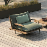 Nami garden armchair frame on a wooden deck, with iroko wood seat and back slats, slim aluminium legs, and teal cushions with green-toned fabric armrests.