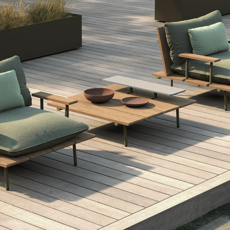 Nami square outdoor coffee table with iroko wood slatted top and slim green aluminium frame, shown on a decked terrace beside green cushioned lounge chairs.