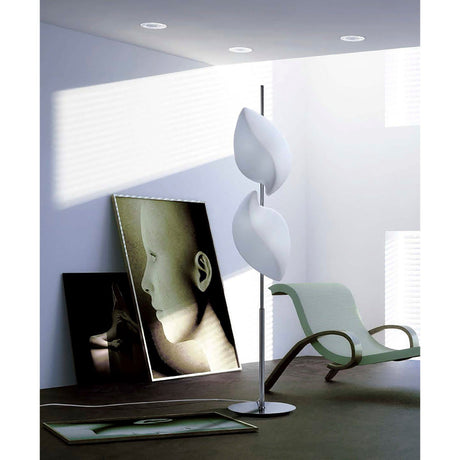 A modern, minimalistic room with the Natura Floor Lamp 4 Light in polished chrome and opal white, a curved lounge chair, and framed abstract face artwork leaning against the wall. Soft light filters through window blinds onto the floor.