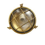 Small Cabin round bulkhead light in raw brass, IP64, with ribbed glass lens and crossed brass cage guard, shown on a plain white background.