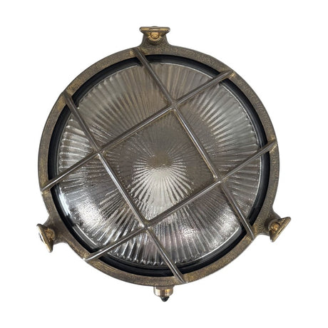 Small round bulkhead light in antique brass with cross grille over ribbed glass, nautical porthole style, shown on a plain white background.