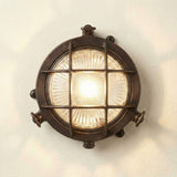 Mini Compass Guard round bulkhead light in antique brass, with crossed-bar grid guard over domed ribbed glass and rim thumb screws, lit against a plain light background.