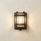 Cargo Outdoor Wall Light in antique brass with ribbed glass panel, lit on a plain light wall, IP64-rated bulkhead fixture with brass bands and side windows.