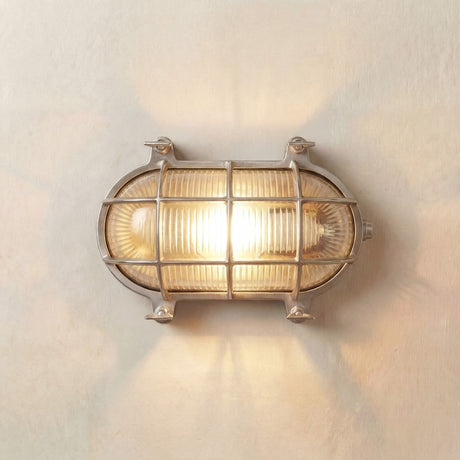 Horatio Oval Bulkhead Light in satin nickel, illuminated on a wall, with ribbed glass, caged bars, and corner lugs, IP64 rated.