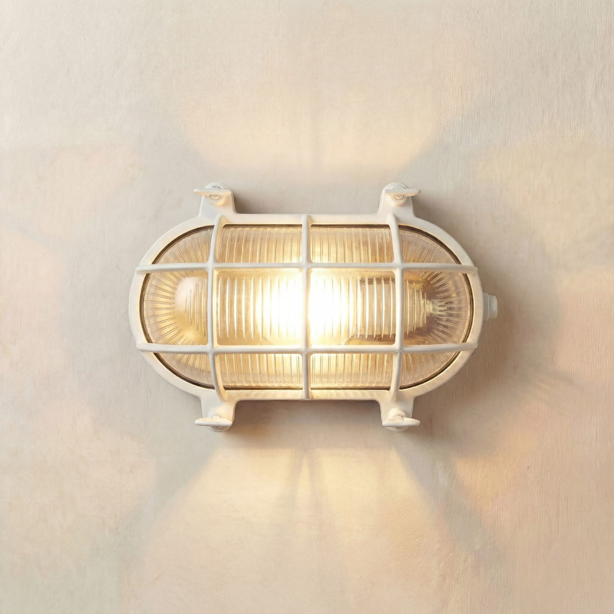 Horatio Oval Bulkhead Light IP64 in white, a brass wall light with ribbed glass diffuser and protective cage, illuminated on a plain wall background.