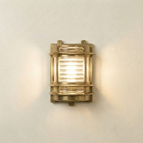 Cargo IP64 outdoor wall light in raw brass, half-round nautical-style fixture with ribbed glass panel and banded brass body, illuminated on a plain light wall.