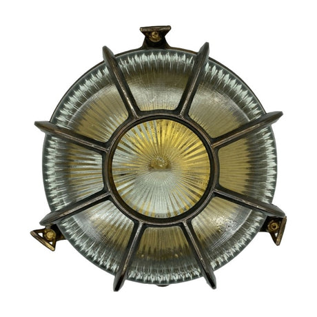 Grand Capstan round bulkhead light in antique brass, with radiating cage bars over ribbed glass and three mounting brackets, shown against a plain white background.
