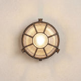 Grand Capstan round bulkhead light in antique brass, with radiating bars over ribbed glass lit from within, mounted on a plain light wall.