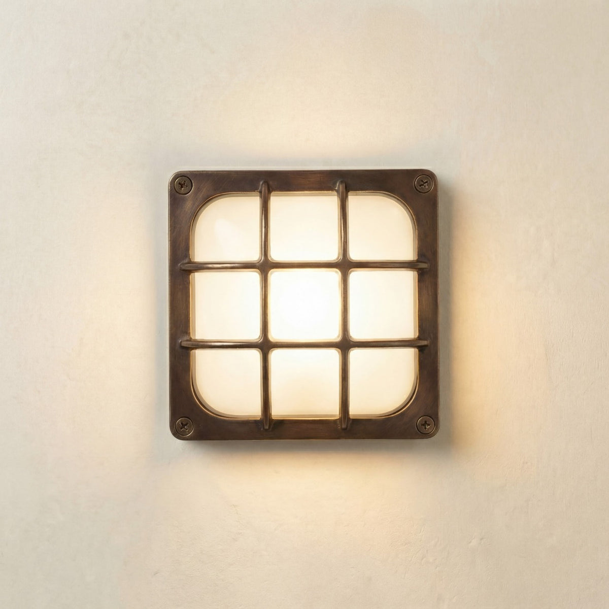 Francis Outdoor Wall Light in antique brass, square bulkhead design with a 3x3 bar guard over frosted glass diffuser, illuminated on a plain light wall, IP64 rated.