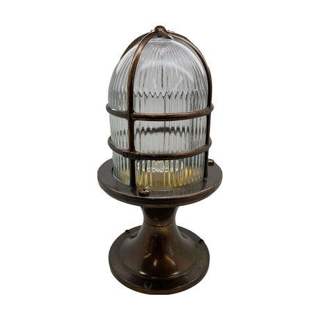 Wellington Grand Outdoor Post Light in antique brass, with a ribbed glass dome encased in a brass bar cage atop a flared pedestal base, shown on a plain white background.