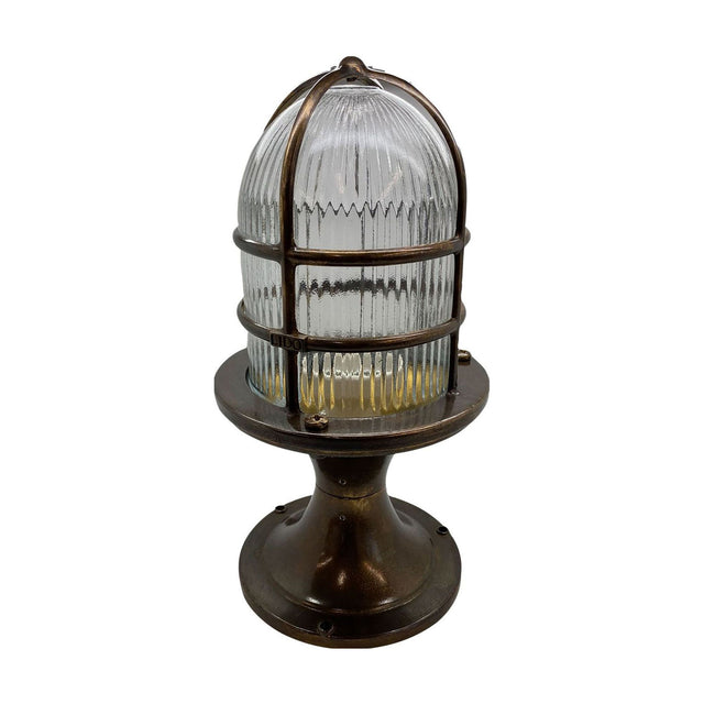 Wellington Grand Outdoor Post Light in antique brass, with a ribbed glass dome encased in a brass bar cage atop a flared pedestal base, shown on a plain white background.