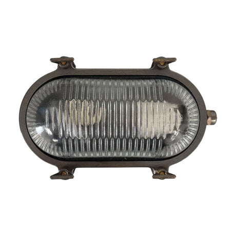 Small Siren oval bulkhead light in antique brass finish with ribbed clear glass cover and four corner screw fixings, shown against a plain white background.