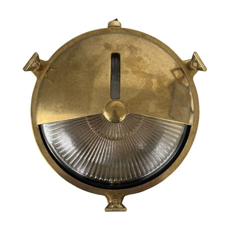 Trident Shield round bulkhead light in raw brass, with a half-moon shield over ribbed glass, slotted light line, and triangular rim lugs, shown on a white background.