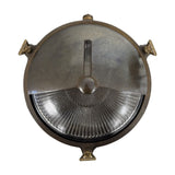 Trident Shield round bulkhead wall light in antique brass, with a half metal shield over ribbed glass and triangular wall brackets, shown on a white background.
