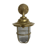 Quinn Guard outdoor wall lantern in raw brass finish, with a round wall plate, curved goose-neck arm, broad hood, and ribbed glass globe wrapped in a brass cage, shown on a white background.
