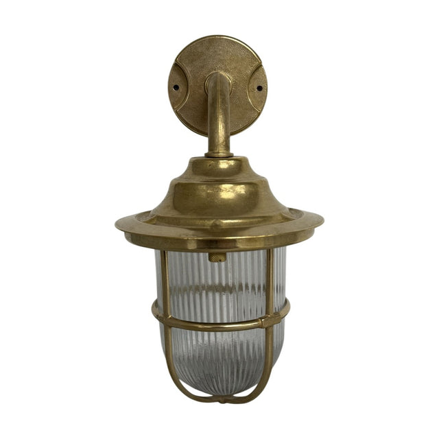 Quinn Guard outdoor wall lantern in raw brass finish, with a round wall plate, curved goose-neck arm, broad hood, and ribbed glass globe wrapped in a brass cage, shown on a white background.