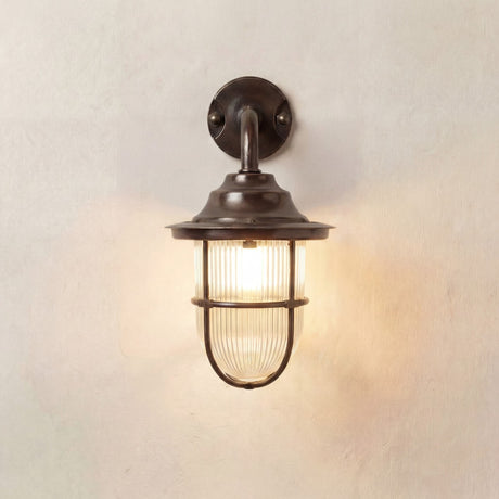 Quinn Guard outdoor wall lantern in antique brass with goose-neck arm, wide hood and ribbed glass shade in a cage guard, lit against a plain light background.
