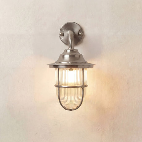 Quinn Guard outdoor wall lantern in satin nickel, goose-neck arm from round wall plate to flared hood over caged ribbed glass shade, lit against a plain light background.