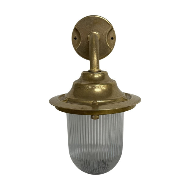 Quinn Outdoor Wall Lantern in raw brass with a gooseneck arm, round wall plate, flared hood and clear ribbed glass dome, IP64 rated, shown on a plain white background.