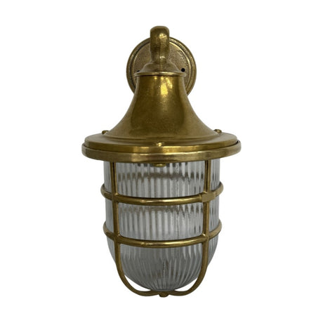 Grand Tiller IP64 outdoor wall lantern in raw brass, with a flared hood, ribbed glass shade, and protective brass cage, shown on a plain white background.