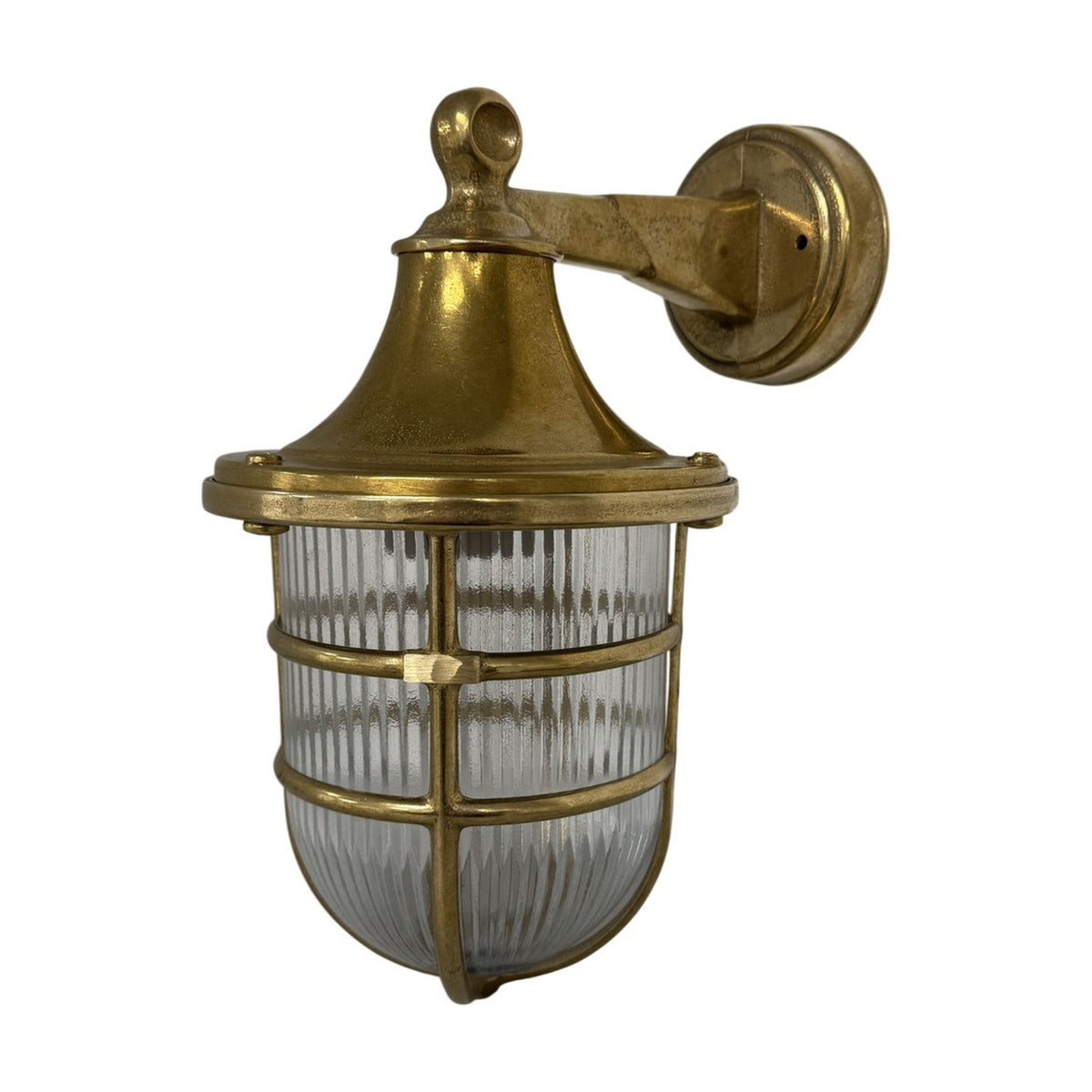 Grand Tiller outdoor wall lantern in raw brass, with flared hood, ribbed glass shade, and brass cage guard on a wall-mounted arm, shown against a plain white background.