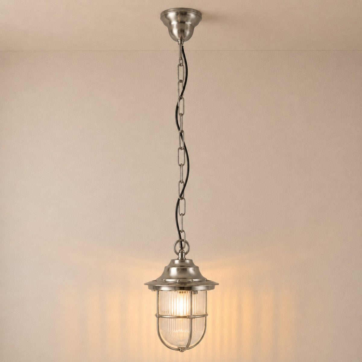 Hull Guard IP54 outdoor pendant light in satin nickel, a caged lantern with ribbed glass shade on a long chain, shown illuminated against a plain light background.