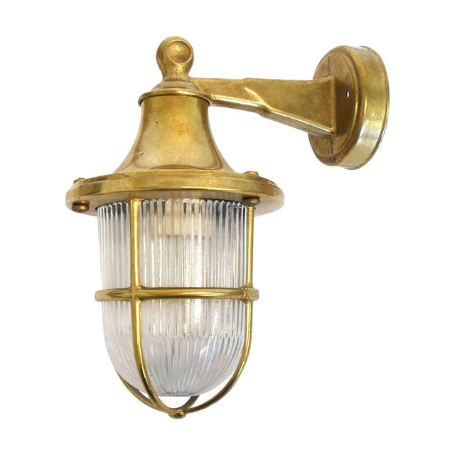 Tiller Outdoor Wall Lantern in raw brass, caged ribbed glass shade with bell-shaped hood on a wall-mounted bracket arm, IP64 rated, shown against a plain white background.