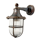 Tiller outdoor wall lantern in Antique Brass, with bell-shaped hood, ribbed glass and protective cage on a bracket arm with round wall plate, shown on a white background.