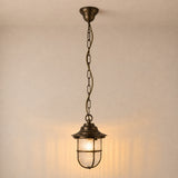 Hull Guard Outdoor Pendant Light in antique brass, a caged lantern with flared hood and ribbed glass shade on a long chain, shown illuminated against a plain wall.