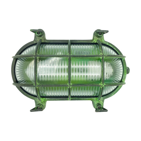 Horatio oval bulkhead light in solid brass with a verdigris finish, protective cage over ribbed glass diffuser, four fixing lugs, IP64 rated, shown on a plain white background.
