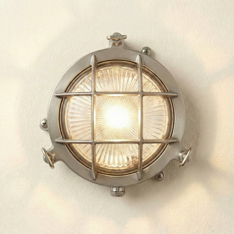 Mini Compass Guard Round Bulkhead Light in satin nickel, a circular outdoor wall light with cross guard over ribbed glass, thumb screws and corner fixing lugs, shown lit on a plain background.