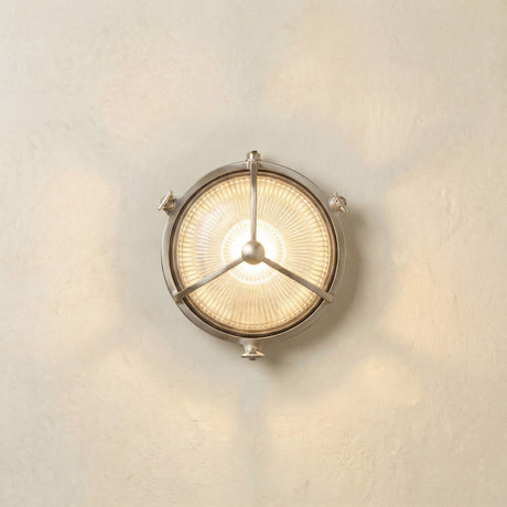 Trident Round Bulkhead Light in satin nickel, a brass outdoor wall light with ribbed glass and a three-arm guard meeting at a central domed boss, shown illuminated on a plain light wall.