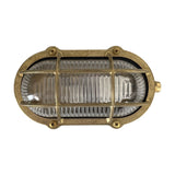 Merchant Oval Bulkhead Light in raw brass, IP64-rated, with a brass cage over ribbed glass and screw-fixed oval frame, shown on a plain white background.