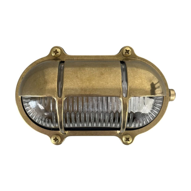 Palaemon oval eyelid bulkhead light in raw brass finish, with ribbed glass lens, brass guard bars, and four corner screws, shown on a plain white background.