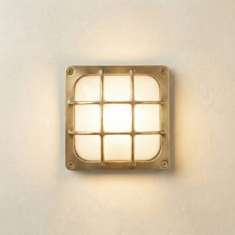 Francis Outdoor Wall Light in raw brass, square bulkhead with nine-pane cage over frosted glass diffuser, corner screws, illuminated on a light wall background.