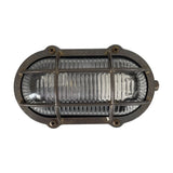 Merchant Oval Bulkhead Light in antique brass with ribbed glass and protective cage, secured by four corner screws, IP64 rated, shown on a plain white background.
