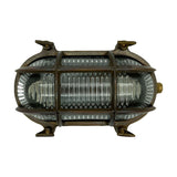 Horatio Junior oval bulkhead light in antique brass, with a crossed brass cage guarding ribbed glass and four wall-fixing lugs, shown on a plain white background.