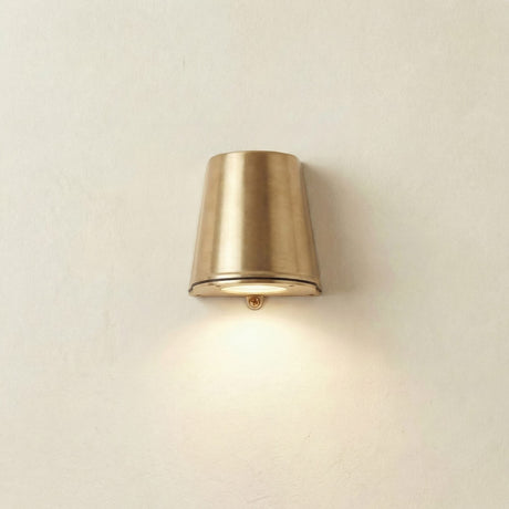 Mast Outdoor Wall Light IP65 in raw brass, a tapered cone downlight on a flat flanged base, mounted on a plain light wall and illuminated.