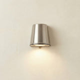 Mast Outdoor Wall Light IP65 in satin nickel, a tapered brass cylinder on a light wall, casting downward light through its base, IP65 rated.