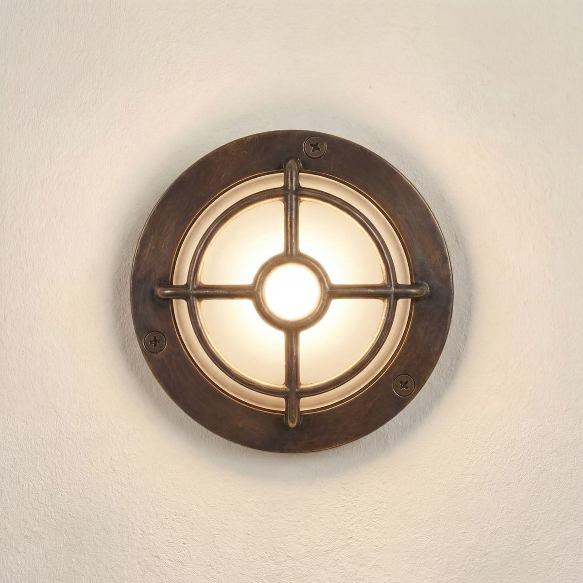 Walkway Guard Outdoor Wall Light in antique brass, a round IP65 fixture with cross-and-ring guard over a frosted glass diffuser, mounted on a light wall.