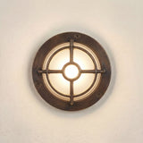 Walkway Guard Outdoor Wall Light in antique brass, a round IP65 fixture with cross-and-ring guard over a frosted glass diffuser, mounted on a light wall.