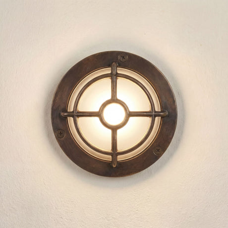 Walkway Guard Outdoor Wall Light in antique brass, a round IP65 fixture with cross-and-ring guard over a frosted glass diffuser, mounted on a light wall.